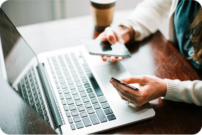woman sitting in front of a laptop holding a phone in one hand and a credit card in the other